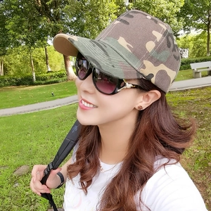 Close-up of a woman wearing a camouflage baseball cap and black cat-eye sunglasses outdoors