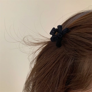 Detailed view of small black velvet flower hair clip worn on long brown hair