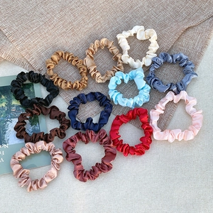 12-piece set of solid color satin scrunchies in various shades on a textured background