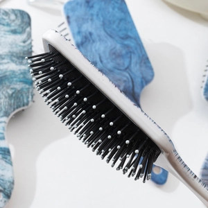 Hair brush with blue water ripple pattern and black bristles on a soft blurred background