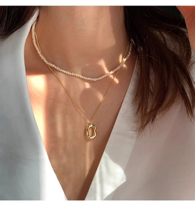 Close-up of double-layer necklace with freshwater pearls and oval gold pendant on model