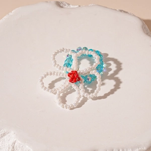 Detailed shot of handmade white flower bead ring and blue crystal band on stone tray