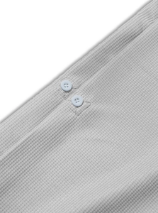 Dettaglio macro della trama a nido d'ape grigio chiaro e bottoni di una polo da uomo