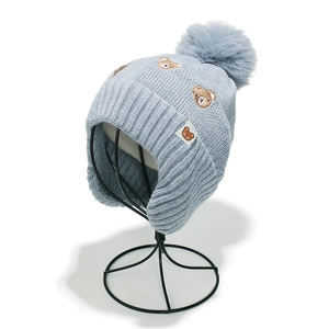 Détail du bonnet en tricot bleu clair pour bébé avec broderie ours et pompon pelucheux