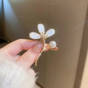 Détail d'une broche fleur dorée avec pétales blancs et perle tenue à la main