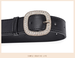 Close-up of black leather belt featuring a large square buckle encrusted with shiny crystals
