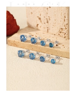 Detail of four pairs of S925 silver stud earrings with round blue stones on stone texture
