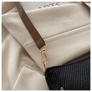 Detail of black woven texture bag with brown leather strap and gold metal hardware