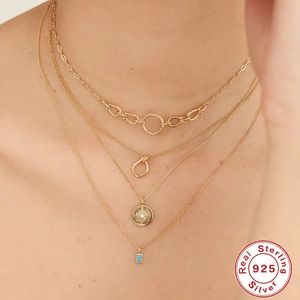 Detail of layered S925 silver necklaces with sun medallion and turquoise stone on model