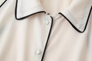 Détail de robe chemise sans manches crème avec liseré noir contrasté et boutons en satin