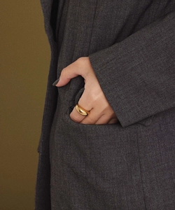 Close-up of a high-polished golden dome ring worn on a finger against a grey blazer