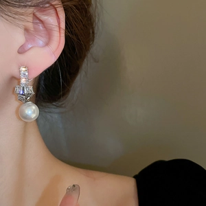 Detail view of crystal-encrusted knot earrings with a dangling white pearl on female model
