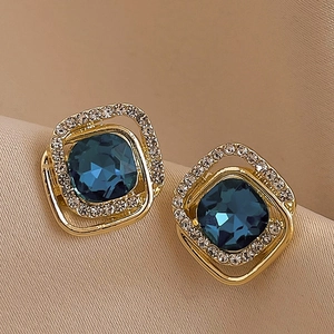 Detail view of retro gold earrings featuring deep blue center stone and white crystals