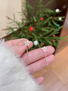 Detailed view of silver snowflake earrings with cubic zirconia held by hand in festive setting