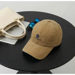 Detailed close-up of khaki corduroy baseball cap with blue HB embroidery on a table