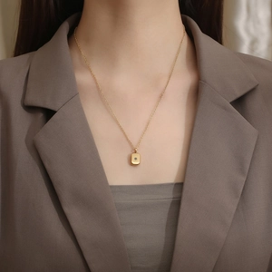 Close-up of a gold rectangle starburst pendant necklace worn with a brown blazer