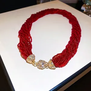 Exaggerated multi-layer red seed bead necklace with a gold crystal-encrusted magnetic clasp
