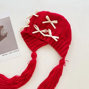 Detailansicht einer roten Strickmütze mit weißen Satinschleifen und langen Quasten
