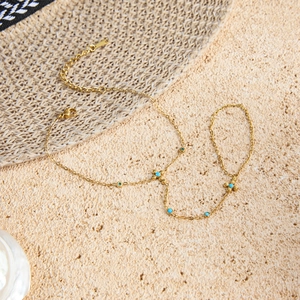 Detail eines Goldketten-Handarmbands mit Türkisperlen auf strukturiertem Grund