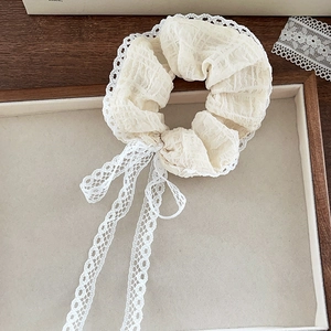 Detailed shot of cream lace scrunchie with long ribbons on a wooden display tray