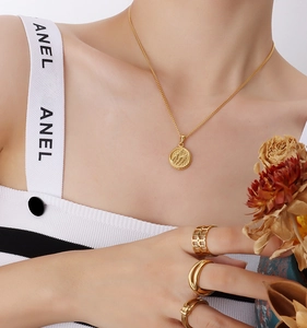 Detail of 18K gold plated wing pendant necklace with textured coin and gold rings on model