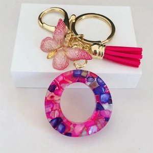 Detail of resin letter O keychain with pink butterfly charm and magenta tassel on stand