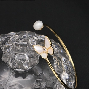 Detail of golden open bangle with white shell butterfly and pearl on glass texture
