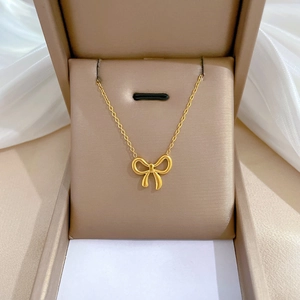 Close-up of golden bow pendant necklace with O-chain in elegant beige jewelry box