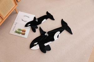 Top view of two sizes of plush orca whale toys on a soft beige carpet in a home setting