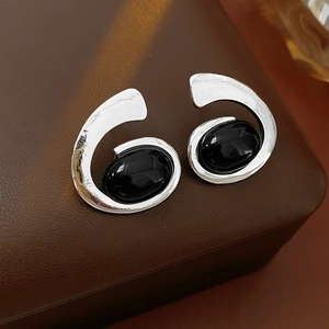 Close-up of silver geometric spiral earrings with black oval gemstones on leather