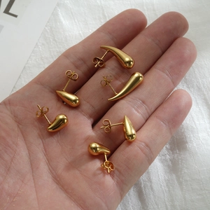 Macro view of gold teardrop earring set in various sizes held by hand on white fabric