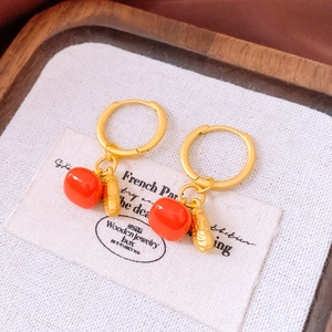 Detail of gold huggie earrings featuring orange bead and textured peanut pendants
