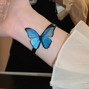Close-up of a blue glitter butterfly bracelet with black strap on wearer wrist
