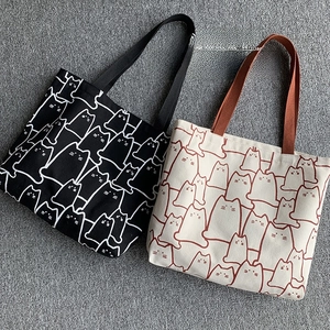 Detailed view of canvas tote bags with cute cartoon cat prints in black and beige colors