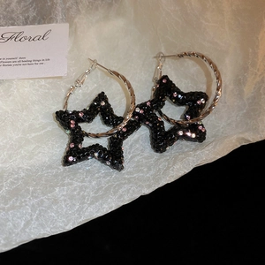 Détail de boucles d'oreilles en étoile avec strass noirs et anneaux évidés style Y2K