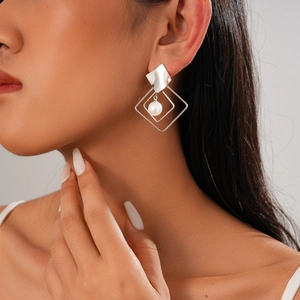 Close-up of a silver geometric hollow rhombus earring with a hanging white pearl drop
