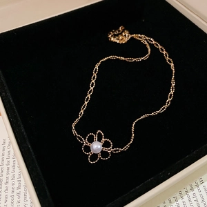 Detailed close-up of a gold hollow flower pendant with a white pearl in a black velvet box