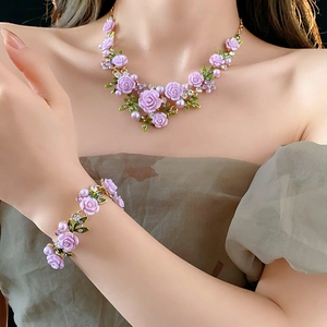 Détail d'un ensemble collier et bracelet doré avec roses mauves et perles sur modèle