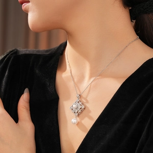 Macro view of a silver floral rhombus pendant with zircon and a hanging white pearl