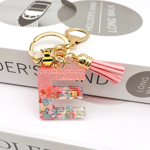 Detail of pink resin letter E keychain with gold bee charm and suede tassel accessory