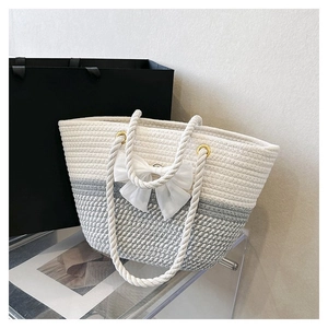 Detail of woven tote with beige and grey pattern, white bow, and gold metal rings
