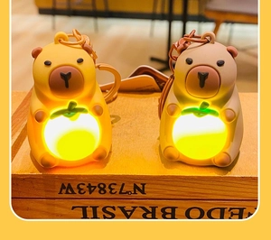 Glow-in-the-dark capybara plush keychains in yellow and brown on vintage wood base