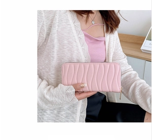 Detail of pink long wallet with wavy texture and gold zipper held by hand