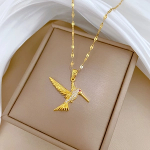 Macro shot of gold hummingbird pendant with clear crystals and a red stone eye on silk