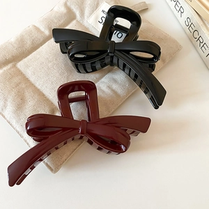 Detailed view of black and dark red bow-shaped hair claws on a beige linen bag background