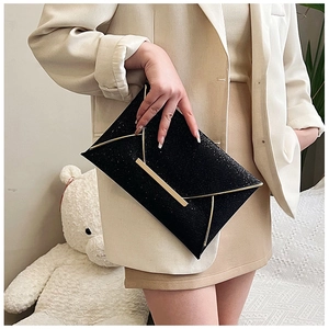 Pochette enveloppe noire scintillante avec bordure dorée portée par un mannequin chic