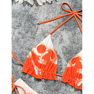 Lace-up triangle bikini top with skull print and ruffled hem on a textured stone surface