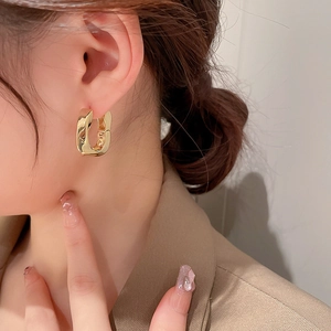 Gros plan de boucles d'oreilles créoles torsadées en forme de U dorées sur un mannequin