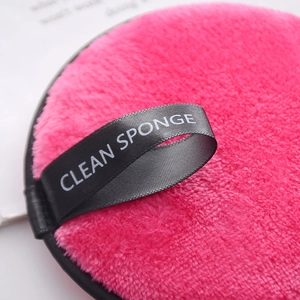 Pink microfiber reusable makeup remover puff with a black hanging loop and soft texture