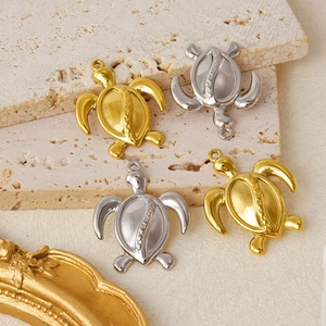 Detailed close-up of gold and silver sea turtle pendants on a textured beige stone surface
